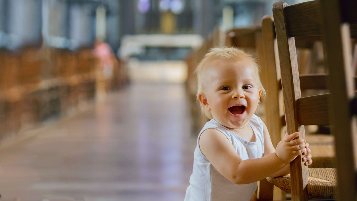 Toddler holding on to a chair in the back of a church