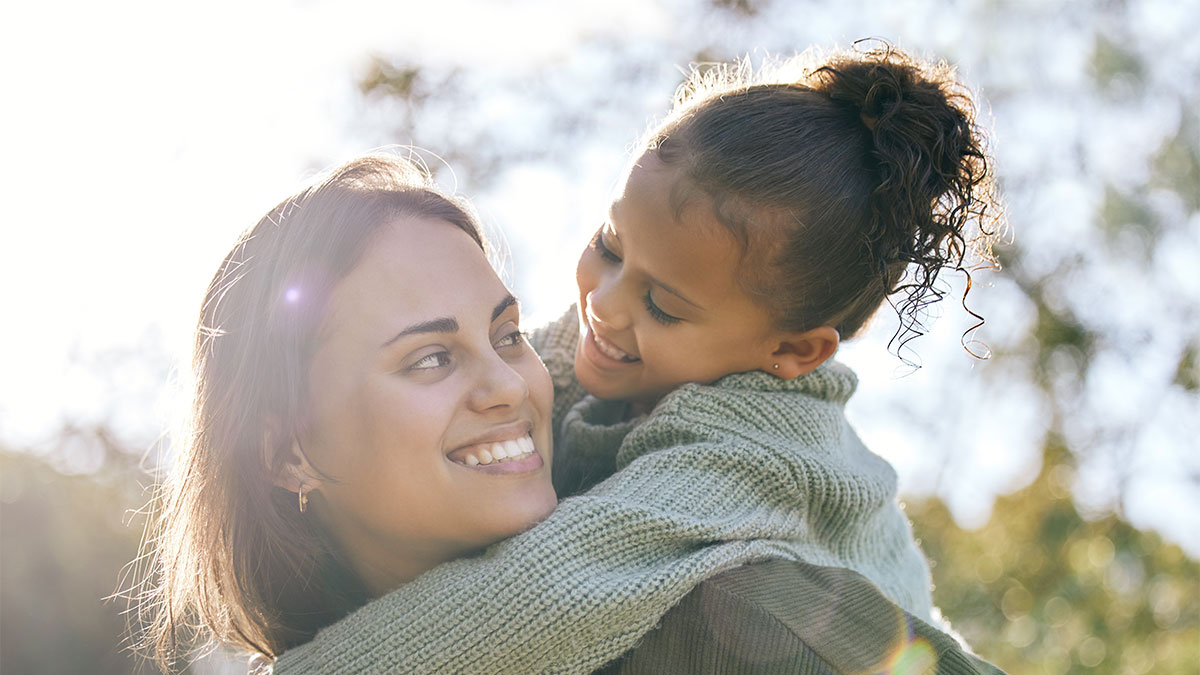 Young mother with her daughter on her back and both are smiling 